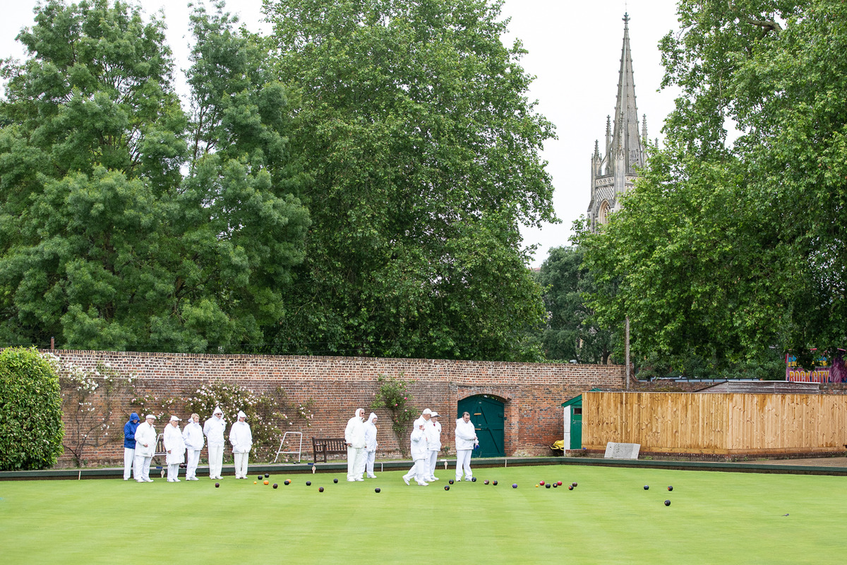 The spire of All Saints Church peers through the backdrop of trees in Higginson Park, almost keeping guard over the bowlers in the rain.